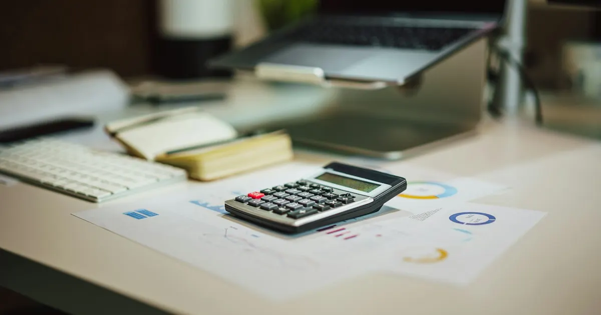 A calculator resting on printed charts next to a laptop on a desk