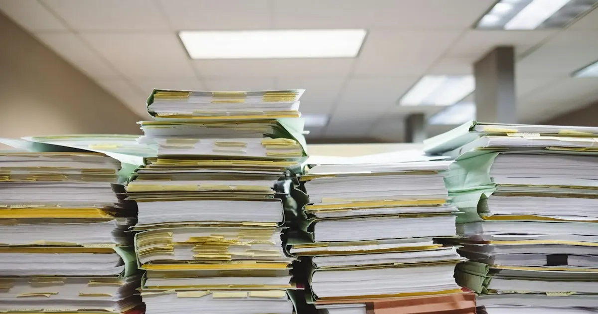 Large stacks of paper files piled on a desk