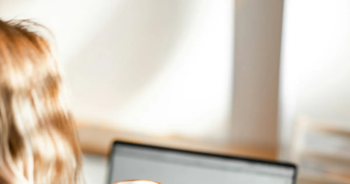 Woman holding a coffee cup while reviewing information on a laptop
